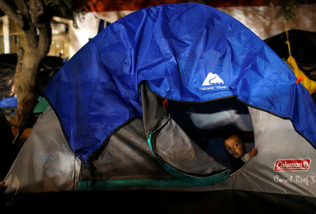 A migrant child, part of a caravan of thousands from Central America trying to reach the United States, takes shelter as he looks out of his family's tent on a street in Tijuana, Mexico, December 7, 2018. REUTERS/Mohammed Salem