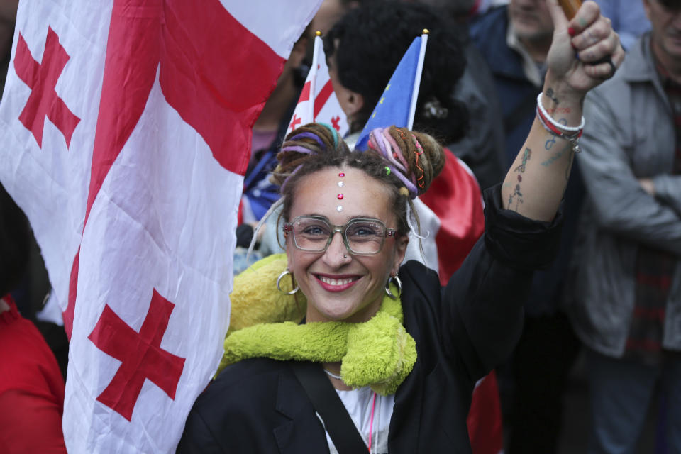 A demonstrator with a Georgian national flag smiles during an opposition protest against foreign influence bill and celebrating of the Independence Day, in the center of in Tbilisi, Georgia, Sunday, May 26, 2024. The opposition has denounced the bill as "the Russian law," because Moscow uses similar legislation to crack down on independent news media, nonprofits and activists critical of the Kremlin. (AP Photo/Zurab Tsertsvadze)