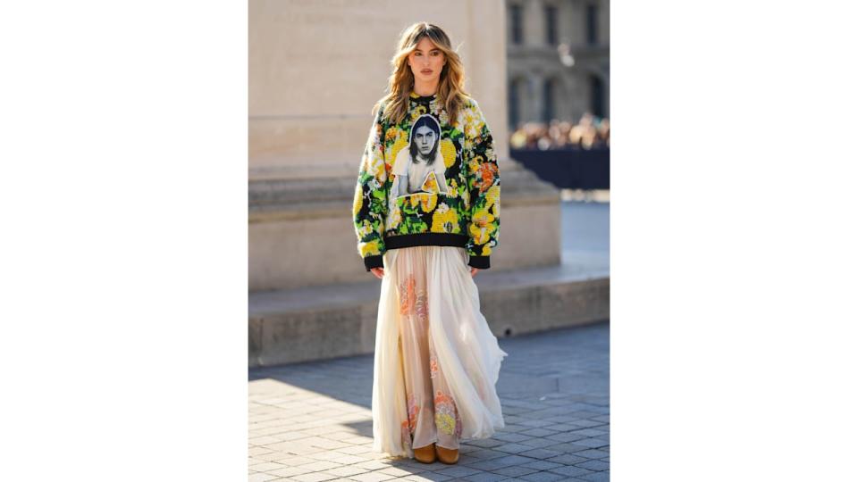 Eve Jobs wears a yellow / green / white / orange braided wool with white and black face print pattern oversized sweater from Louis Vuitton, white pleated / accordion tulle long skirt, camel shiny leather pointed heels shoes , outside Louis Vuitton, during Paris Fashion Week - Womenswear Spring/Summer 2023, on October 04, 2022 in Paris, France