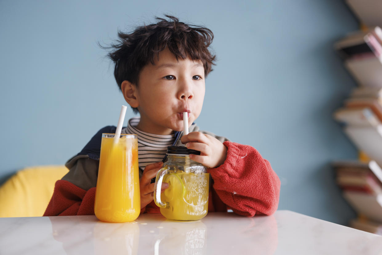 A little asian boy, about 4 years old, wearing a red sweater, was drinking juice