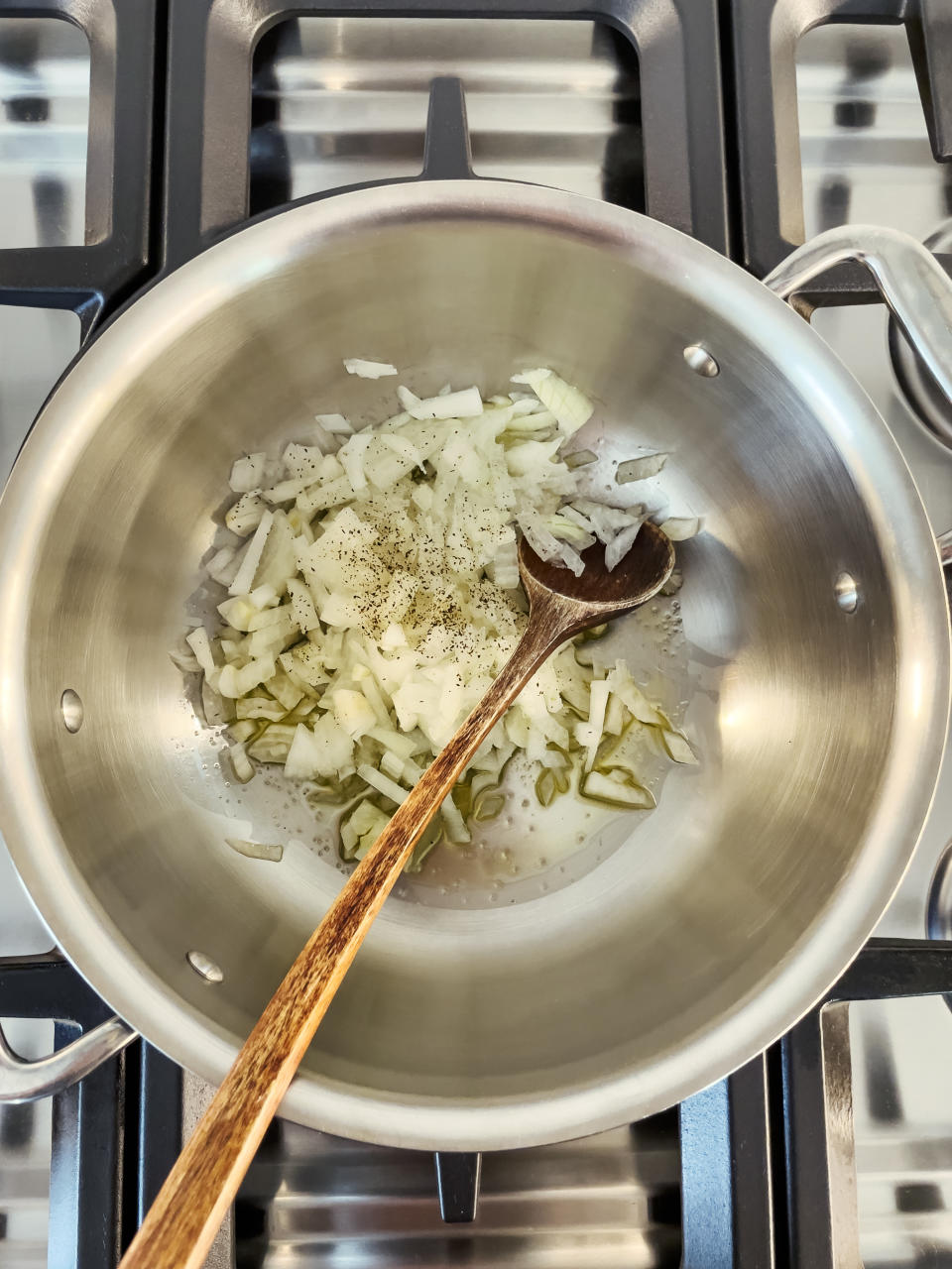 Chopped onions being sautéed in a pot on a stove with a wooden spoon