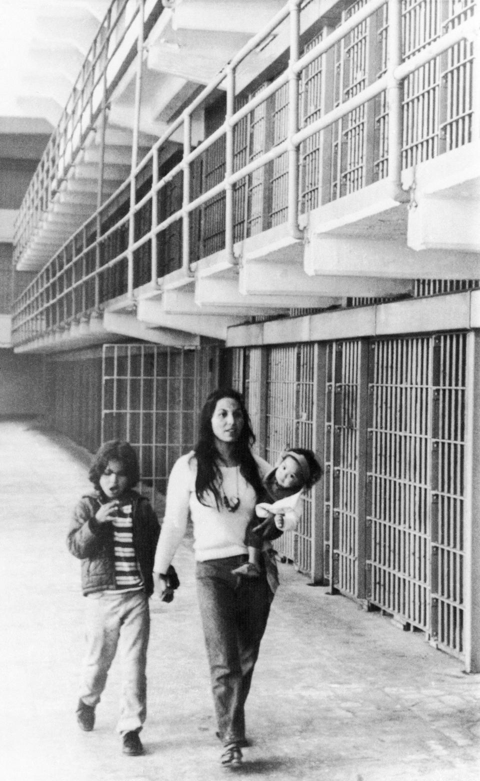 In this photo taken March 26, 1970, Eldy Bratt, 33, walks down the lonely corridor of a cell block on Alcatraz with her son Peter Bratt, left, and one of her daughters in San Francisco. The week of Nov. 18, 2019, marks 50 years since the beginning of a months-long Native American occupation at Alcatraz Island in the San Francisco Bay. The demonstration by dozens of tribal members had lasting effects for tribes, raising awareness of life on and off reservations, galvanizing activists and spurring a shift in federal policy toward self-determination. (AP Photo/Richard Drew, File)