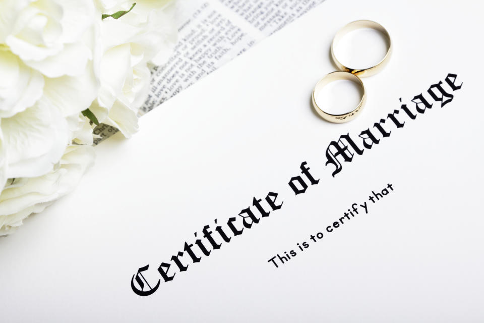 A certificate of marriage with wedding rings and flowers on top of it