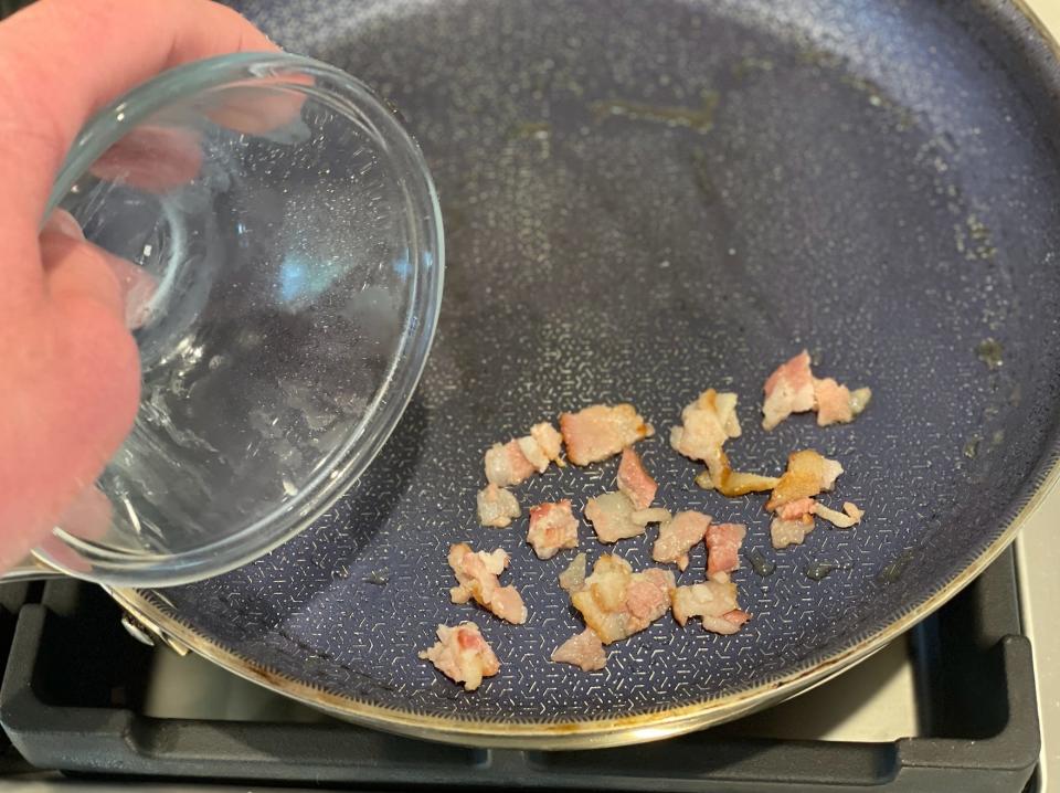 hand pouring pieces of bacon into a frying pan