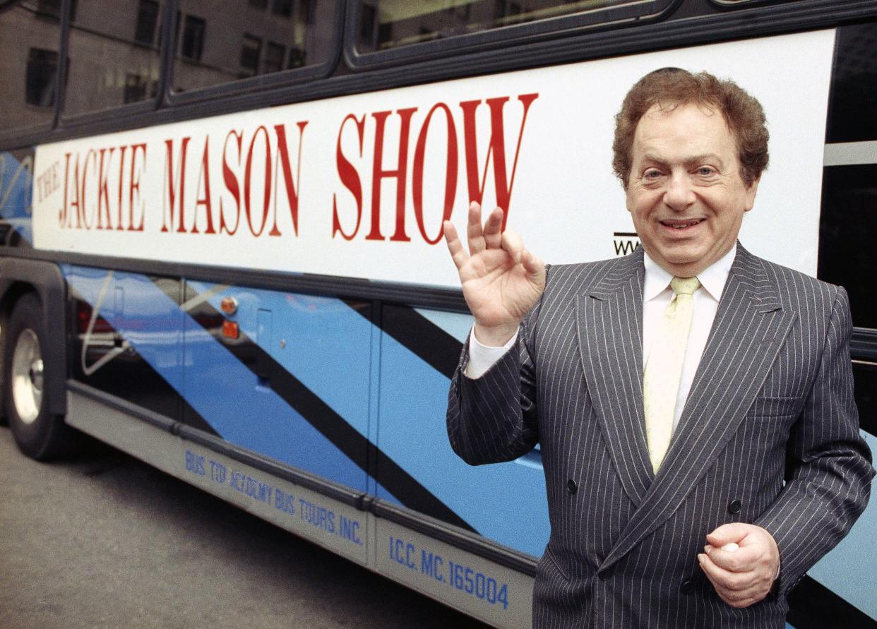 Actor/comedian Jackie Mason stands beside a bus displaying a sign advertising his TV show in 1992. 