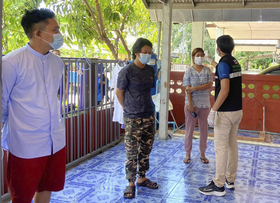 In this photo released by the San Sai District Administrative Office, a Thai officer checks the temperature of journalists working for Democratic Voice of Burma, at San Sai District in Chiang Mai province north of Thailand Sunday, May 9, 2021. Three senior journalists working for the online and broadcast news agency in Myanmar who fled after the military government ordered its operations to stop have been arrested by police in northern Thailand, their editor said Monday. (San Sai District Administrative Office via AP)