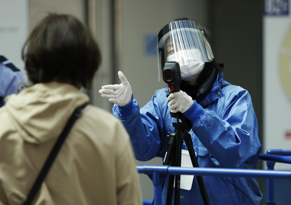 A worker directs a spectator to a next step to enter the arena after taking the person's temperature during the coronavirus pandemic before the ISU World Team Trophy figure skating competition in Osaka, western Japan on April 15, 2021. The picture is still grim in parts of Europe and Asia as variants of the virus fuel an increase in new cases and the worldwide death toll closes in on 3 million. (AP Photo/Hiro Komae, File)