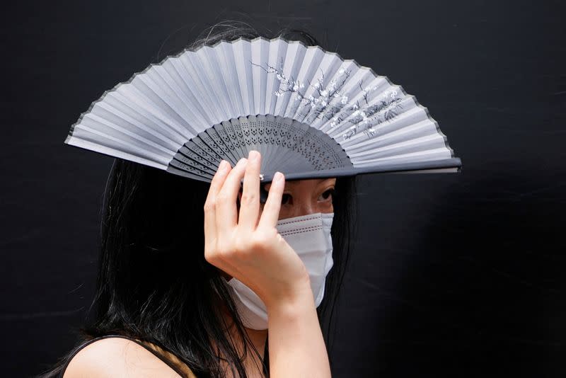 A woman walks on a street as she shields herself from the sun with a fan, amid an alert for heatwave in Shanghai