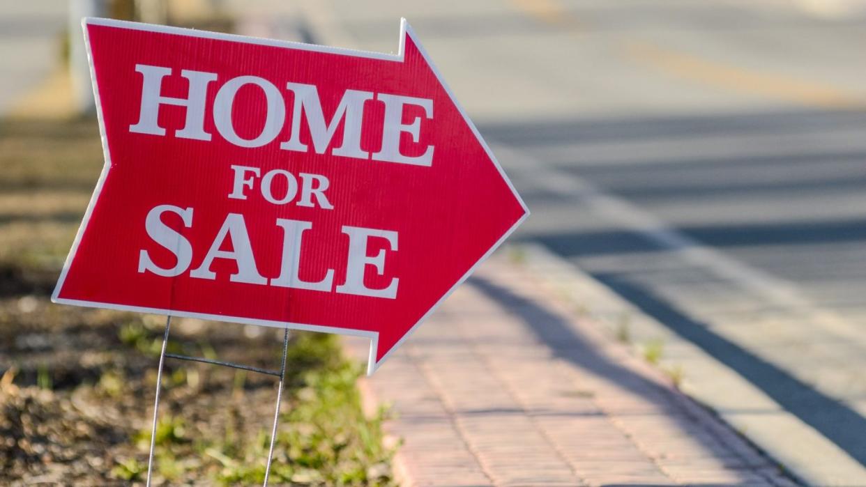 A home for sale sign pointing directing people to a house for sale.