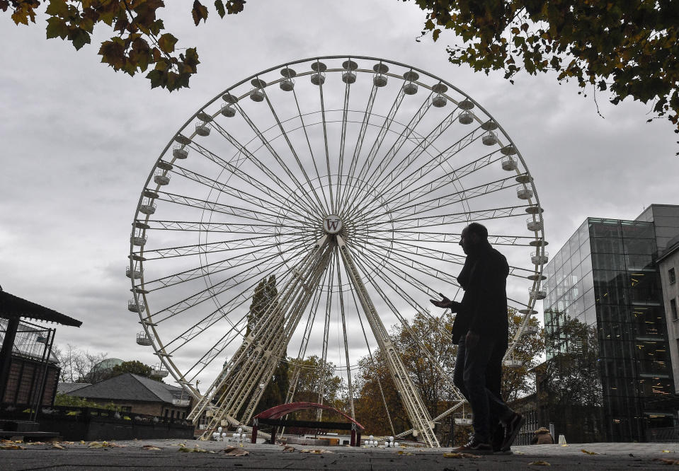 A man passes a closed Ferris wheel in the city center of Essen, Germany, Monday, Nov. 2, 2020. A one month long partial lockdown due to the coronavirus pandemic becomes effective in Germany on Monday. (AP Photo/Martin Meissner)