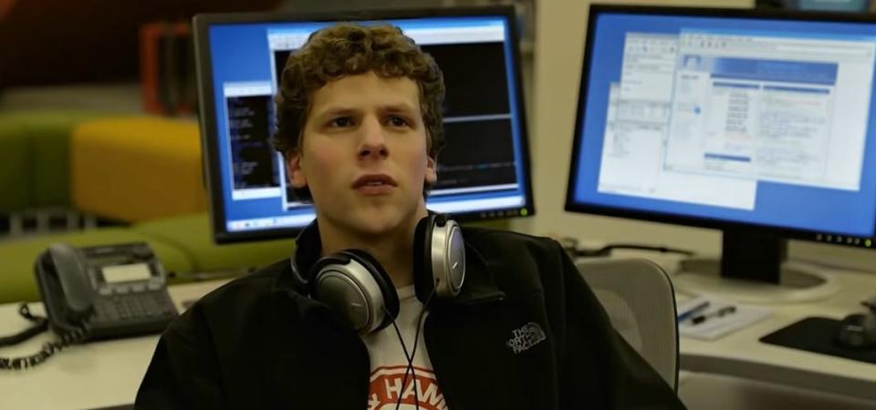 Mark sitting at a desk with headphones around his neck in "The Social Network"