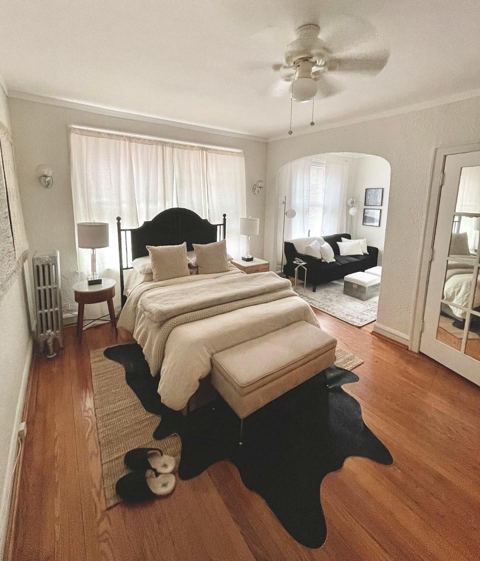 The writer's bedroom with a white bed in the center with a dark headboard, a white storage ottoman bench in front, and a black rug beneath