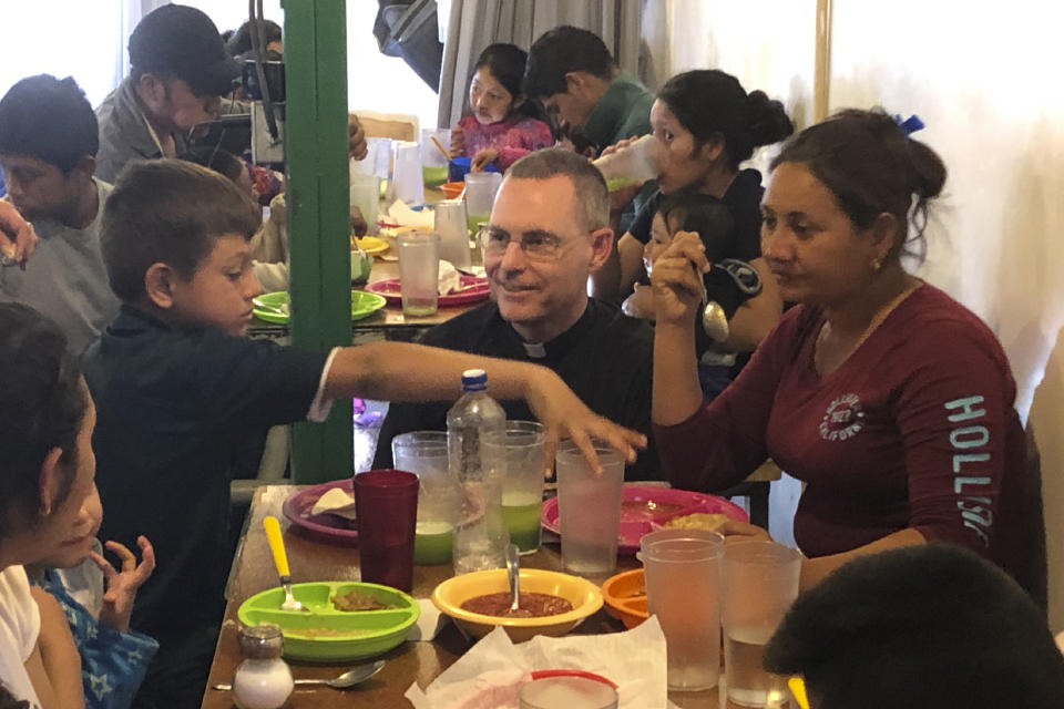 In this Feb. 20, 2020 photo, Jesuit priest Sean Carroll joins a group of asylum-seekers from Honduras in the cafeteria of a migrant-outreach center that his organization, the Kino Border Initiative, operates near the U.S.-Mexico border in Nogales, Mexico. Before the coronavirus gained global attention, Carroll's agency opened the facility just inside the Mexican border. Carroll — who works full-time in Mexico — hoped to expand a twice-daily meal service but now amid worries about COVID-19, neither venue is being used as a dining hall. Instead, migrants line up outside the two buildings and approach the doors one at a time. (AP Photo/David Crary)