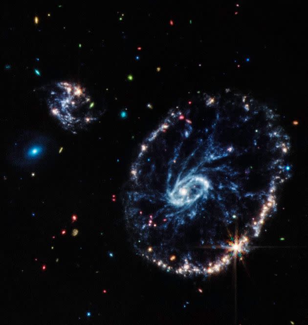 This image from Webb's Mid-Infrared Instrument (MIRI) shows a group of galaxies, including a large distorted ring-shaped galaxy known as the Cartwheel. The Cartwheel Galaxy, located 500 million light-years away in the Sculptor constellation, is composed of a bright inner ring and an active outer ring. While this outer ring has a lot of star formation, the dusty area in between reveals many stars and star clusters.The mid-infrared light captured by MIRI reveals fine details about these dusty regions and young stars within the Cartwheel Galaxy, which are rich in hydrocarbons and other chemical compounds, as well as silicate dust, like much of the dust on Earth.Young stars, many of which are present in the bottom right of the outer ring, energize surrounding hydrocarbon dust, causing it to glow orange. On the other hand, the clearly defined dust between the core and the outer ring, which forms the spokes that inspire the galaxy's name, is mostly silicate dust. The smaller spiral galaxy to the upper left of Cartwheel displays much of the same behavior, showing a large amount of star formation. (Photo: NASA, ESA, CSA, STScI, Webb ERO Production Team)