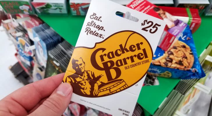 Cracker Barrel gift card in a hand over a shelves with different giftcards