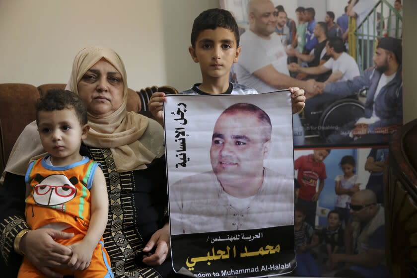 FILE - Amal el-Halabi holds her grandson Fares while her grandson Amro, 7, holds a picture of his father Mohammed el-Halabi, Gaza director of the international charity World Vision, who is detained and accused by Israeli security of diverting sums to Hamas that exceed its total budget, at his family house in Gaza City, Aug. 8, 2016. The Israeli district court in the southern Israeli city of Beersheba found Mohammed el-Halabi guilty of several terrorism charges on Wednesday, June 15, 2022. He has not yet been sentenced. Arabic on the picture reads, " the man of humanity." (AP Photo/Adel Hana, File)