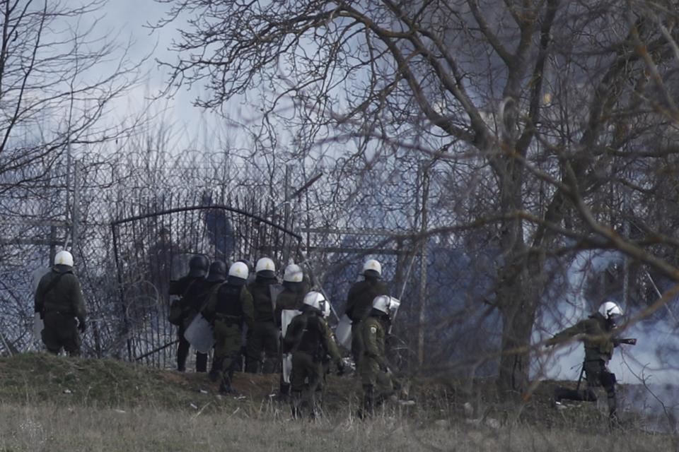 Greek police guard as migrants gather at a border fence on the Turkish side, during clashes at the Greek-Turkish border in Kastanies, Evros region, on Saturday, March 7, 2020. Thousands of refugees and other migrants have been trying to get into EU member Greece in the past week after Turkey declared that its previously guarded borders with Europe were open. (AP Photo/Giannis Papanikos)