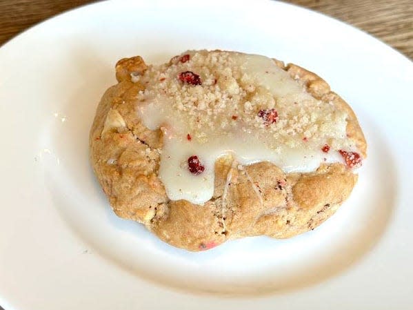 A vanilla cookie topped with white frosting and crumbs on a white plate.