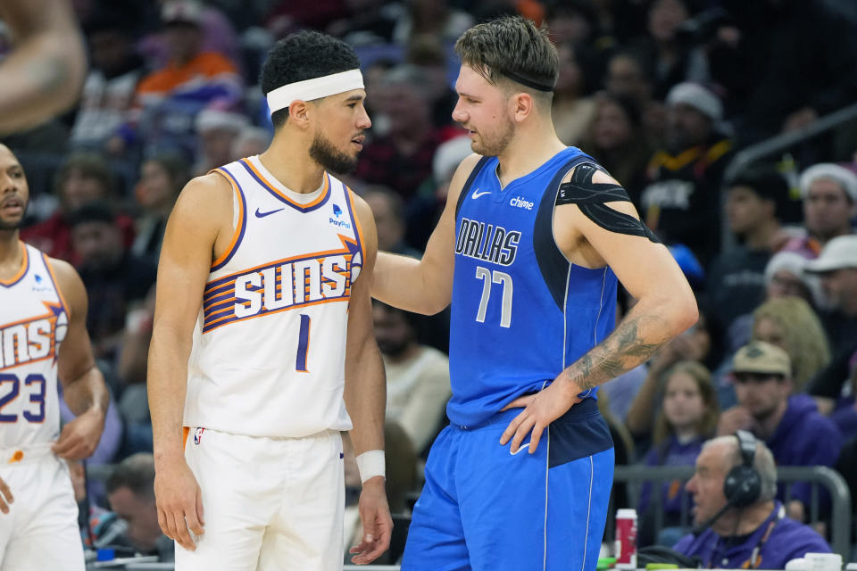 Phoenix Suns guard Devin Booker (1) and Dallas Mavericks guard Luka Doncic (77) talk during the first half of an NBA basketball game, Monday, Dec. 25, 2023, in Phoenix. (AP Photo/Rick Scuteri)