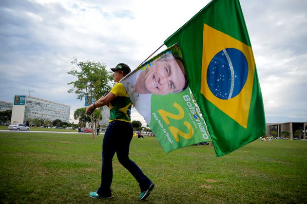 A woman holds a Brazilian flag and another with the image of Brazilian President Jair Bolsonaro, who is running for another term, after general election polls closed in Brasilia, Brazil, Sunday, Oct. 2, 2022. (Photo: AP Photo/Ton Molina)