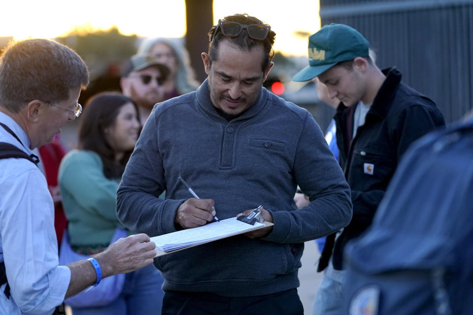 Gilbert Limon signs a petition as he waits in line to enter a voter rally for Independent presidential candidate Robert F. Kennedy Jr., Wednesday, Dec. 20, 2023, in Phoenix. (AP Photo/Matt York)