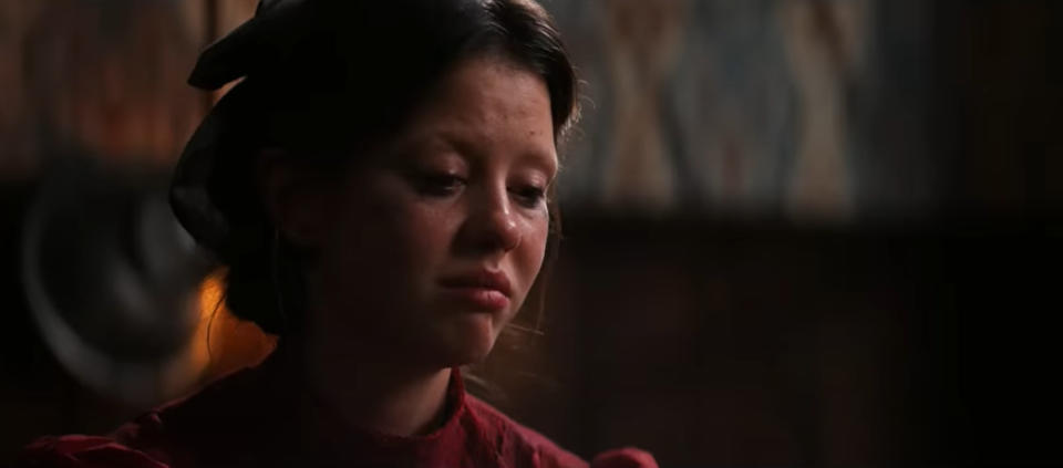 Mia Goth as Pearl has a somber expression and is looking downward.