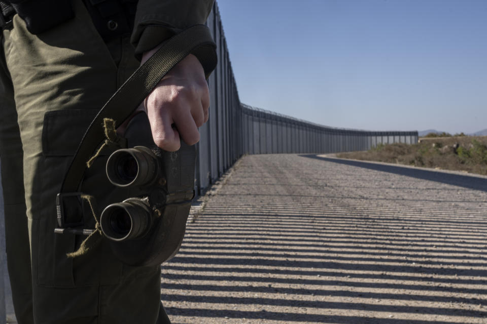 Police border guard holds his benoculars along a border wall near the town of Feres, along the Evros River which forms the the frontier between Greece and Turkey on Sunday, Oct. 30, 2022. Greece is planning a major extension of a steel wall along its border with Turkey in 2023, a move that is being applauded by residents in the border area as well as voters more broadly. (AP Photo/Petros Giannakouris)