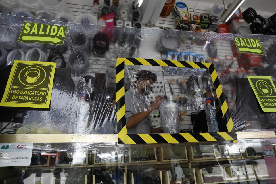 Vendedores en una tienda de electrodomésticos atienden a clientes detrás de una capa de plástico para reducir la propagación del coronavirus en la Ciudad de México, el lunes 6 de julio de 2020. (AP Foto/Rebecca Blackwell)