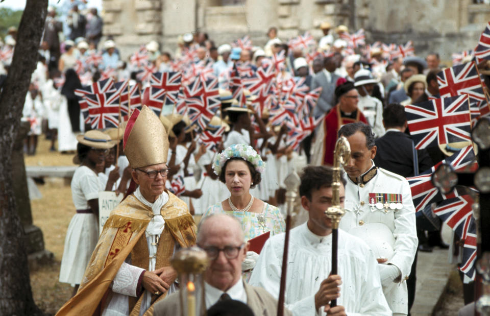 FILE - Britain's Queen Elizabeth II arrives for a church service at St. John's Cathedral, Antigua, Feb. 20, 1966. The Queen is accompanied by the Bishop Knowles, left. After seven decades on the throne, Queen Elizabeth II is widely viewed in the U.K. as a rock in turbulent times. But in Britain’s former colonies, many see her as an anchor to an imperial past whose damage still lingers. (AP Photo, File)