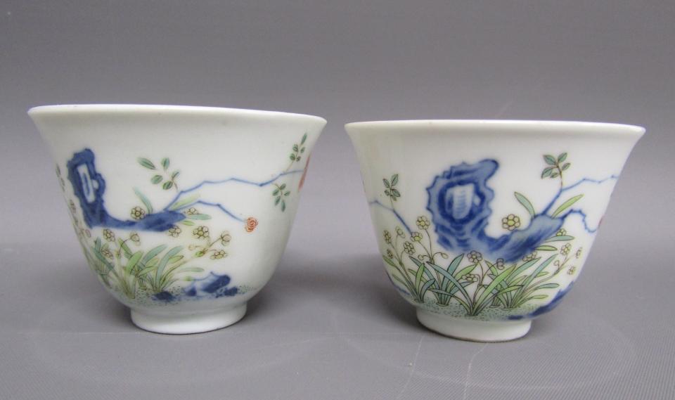 A pair of white porcelain Chinese tea bowls, each decorated with a green and white nature design.