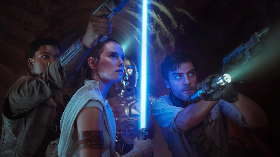 Finn, Rey and Poe brandish weapons as C-3PO looks on in The Rise Of Skywalker.