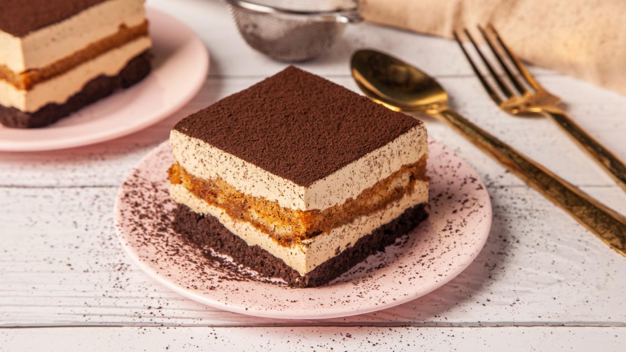  A multi-layered cake on a plate topped with brown dust next to a knife and fork 
