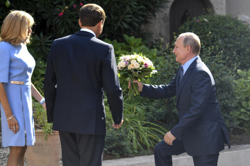 Russian President Vladimir Putin arrives with a bouquet of flowers as French President Emmanuel Macron, center, and his wife Brigitte look on at the fort of Bregancon in Bormes-les-Mimosas, southern France, Monday Aug. 19, 2019. French President Emmanuel Macron and Russian President Vladimir Putin are meeting to discuss the world's major crises, including Ukraine, Iran and Syria, and try to improve Moscow's relations with the European Union. (Gerard Julien, Pool via AP)