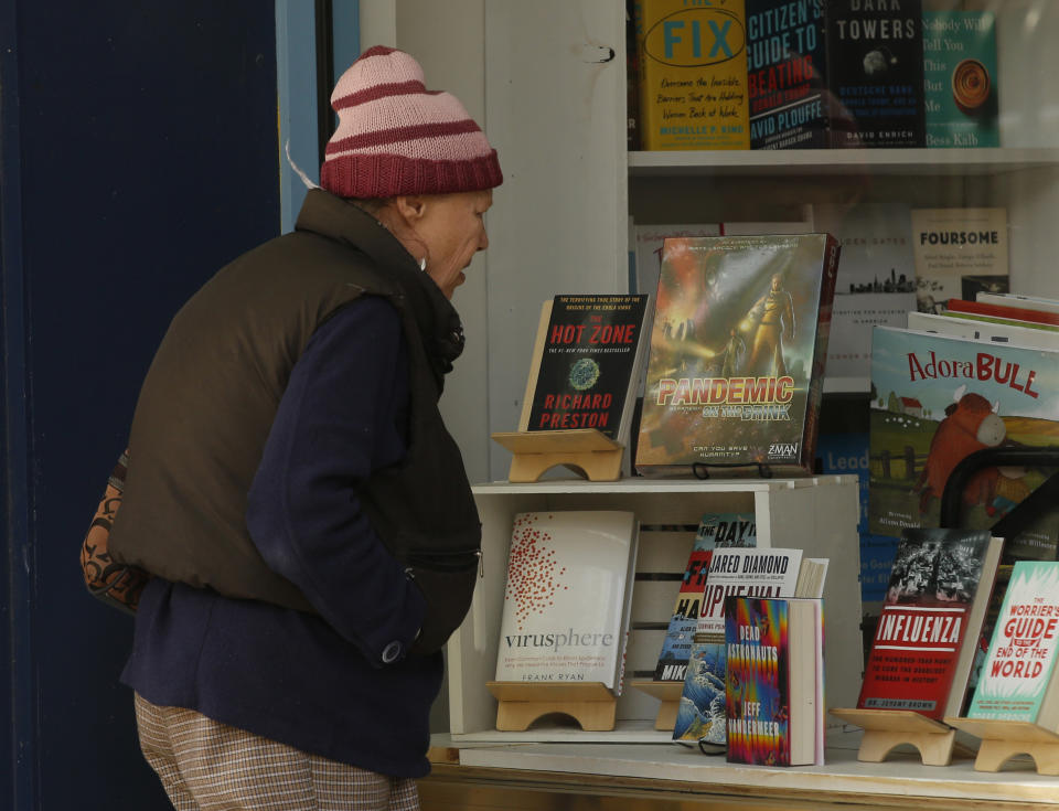 A passer-by pauses to look over the topical books on display at Capital Books, in Sacramento, Calif., Wednesday, March 25, 2020. The shop has been open taking phone orders which they will then mail to or will deliver because of the stay-at-home order due to the coronavirus. Ross Rojek, who co-owns the store with his wife, Heidi, selected a group of timely books, to display in the window, to try to take the edge out of a serious situation. (AP Photo/Rich Pedroncelli)