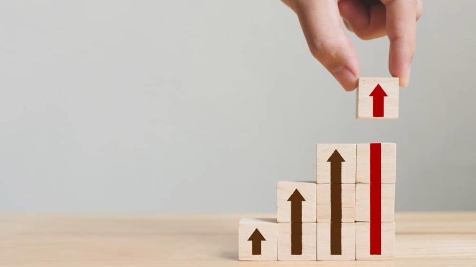 Hand arranging wood block stacking as step stair with arrow up.