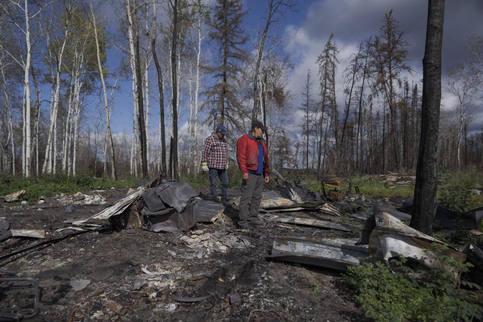 Happy Cardinal, derecha, observa los restos calcinados de su cabaña el domingo 3 de septiembre de 2023, luego de que fue destruida por incendios forestales, cerca de Fort Chipewyan, Canadá. (AP Foto/Víctor R. Caivano)