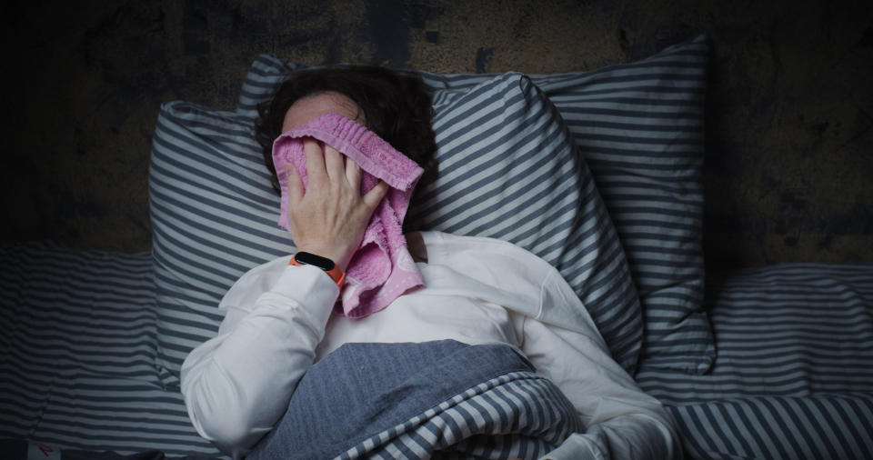 A person wiping sweat from their face while in bed