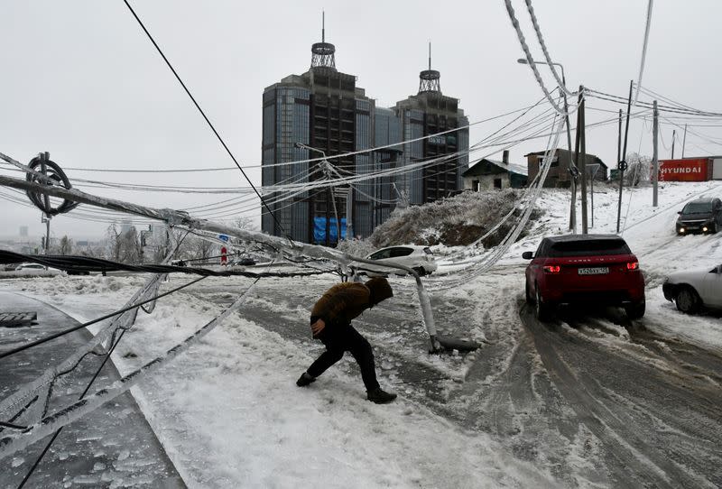 FILE PHOTO: A man walks under a damaged power pole covered with ice after freezing rain in Vladivostok