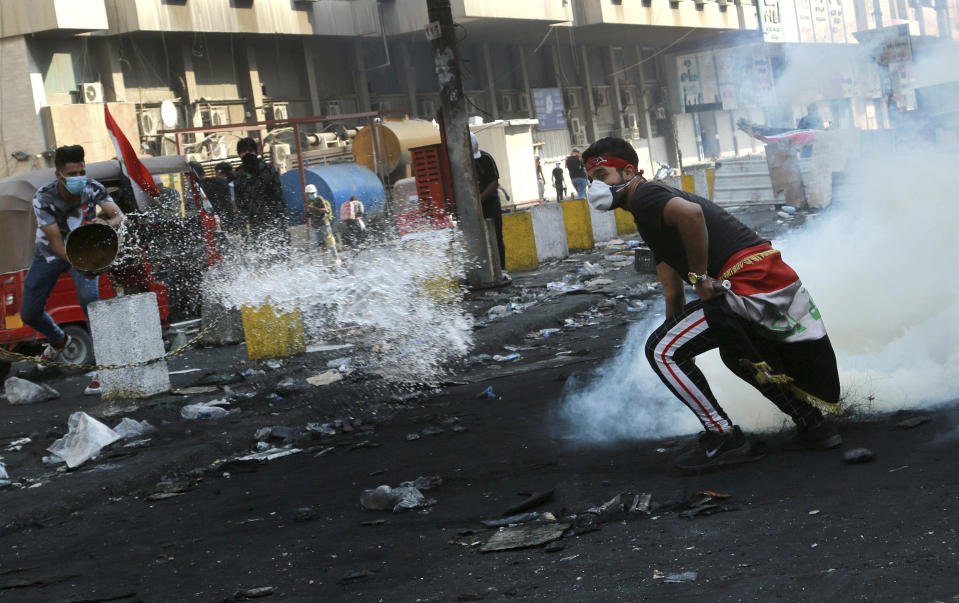 An anti-government protester throws water as another prepares to throw back a tear gas canister fired by police, during ongoing protests in Baghdad, Iraq, Wednesday, Nov. 13, 2019. Protesters say an intensifying crackdown by Iraqi authorities is instilling fears but remain defiant with calls for millions to return to the streets this week. (AP Photo/Hadi Mizban)