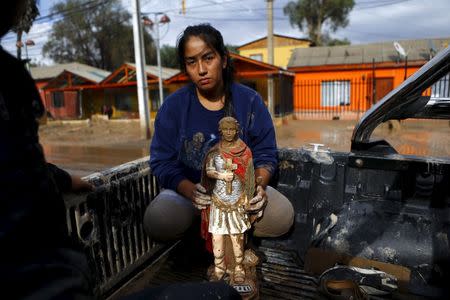 A woman holds a religious figure covered in mud as she is evacuated from her house at Copiapo city, March 26, 2015. REUTERS/Ivan Alvarado