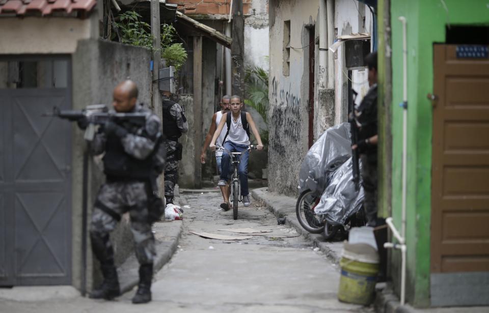 A boy rides a bicycle past police officers taking up positions during an operation at the Mare slums complex in Rio de Janeiro