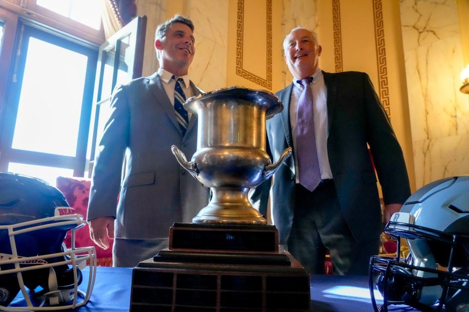 Brown coach James Perry, left, and URI coach Jim Fleming with the Governor's Cup trophy at the State House on Thursday. The teams will meet Saturday at noon in Providence.