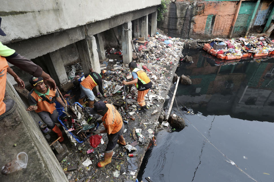 Workers collect trash during a clean-up after flood in Jakarta, Indonesia, Sunday, Jan. 5, 2020. Landslides and floods triggered by torrential downpours have left dozens of people dead in and around Indonesia's capital, as rescuers struggled to search for people apparently buried under tons of mud, officials said Saturday. (AP Photo/Tatan Syuflana)