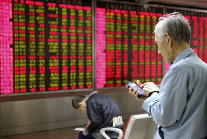 An investor looks at his mobile phone in front of an electronic board showing stock information at a brokerage house in Beijing, China, November 16, 2015. REUTERS/Li Sanxian