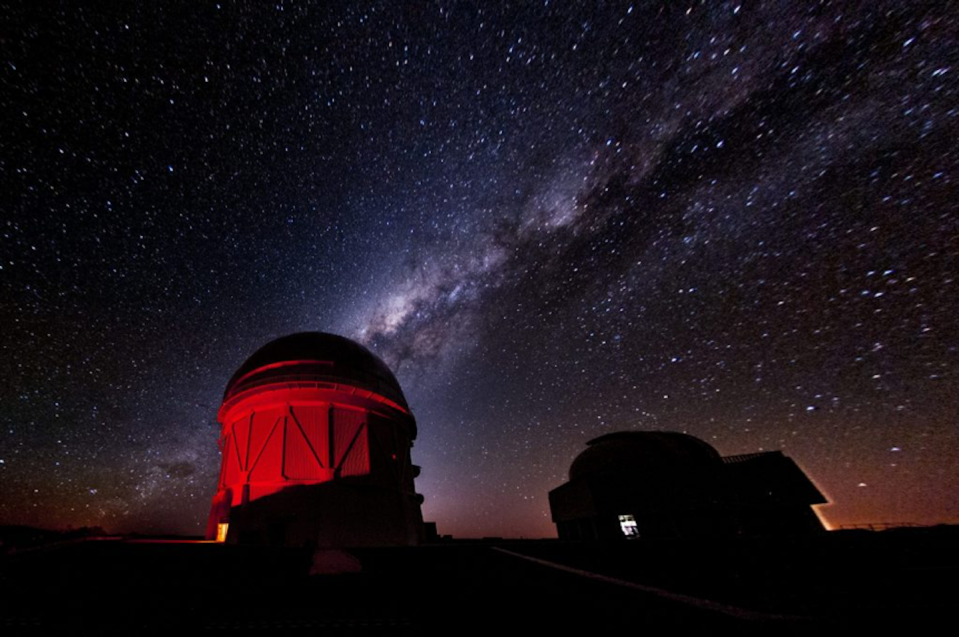 Una foto del edificio de un observatorio iluminado en rojo con el cielo estrellado de fondo.