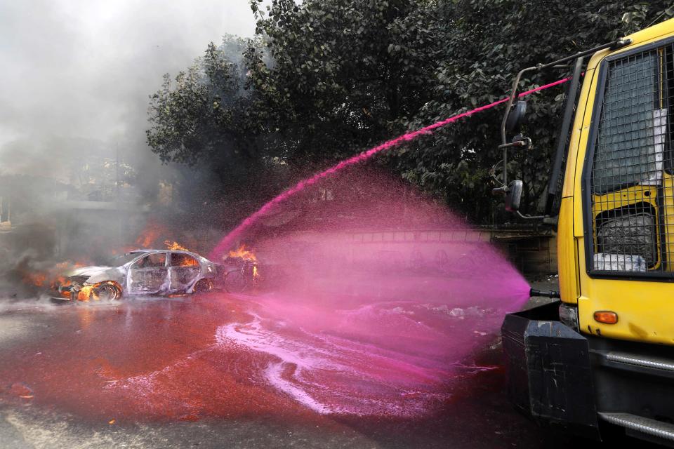 A police vehicle uses colored water to put out flames of a burning vehicle during clashes between police and Jamaat-e-Islami party activists in Dhaka