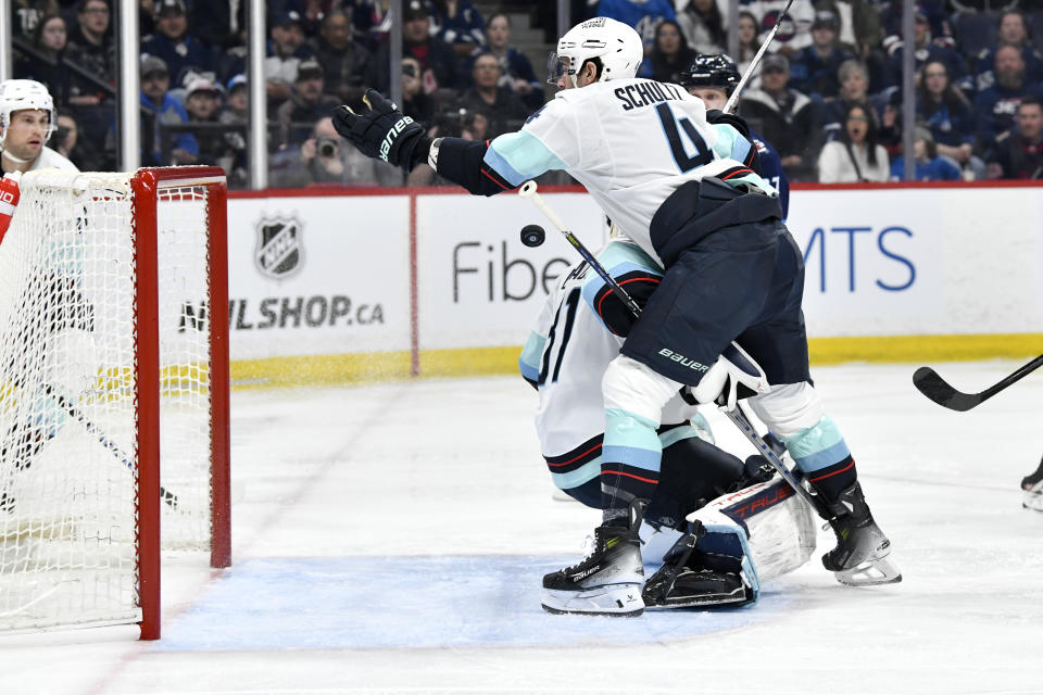 Seattle Kraken's Justin Schultz (4) reaches for a loose puck behind goaltender Philipp Grubauer (31) after a shot by the Winnipeg Jets during the second period of an NHL hockey game in Winnipeg, Manitoba on Tuesday April 16, 2024. (Fred Greenslade/The Canadian Press via AP)