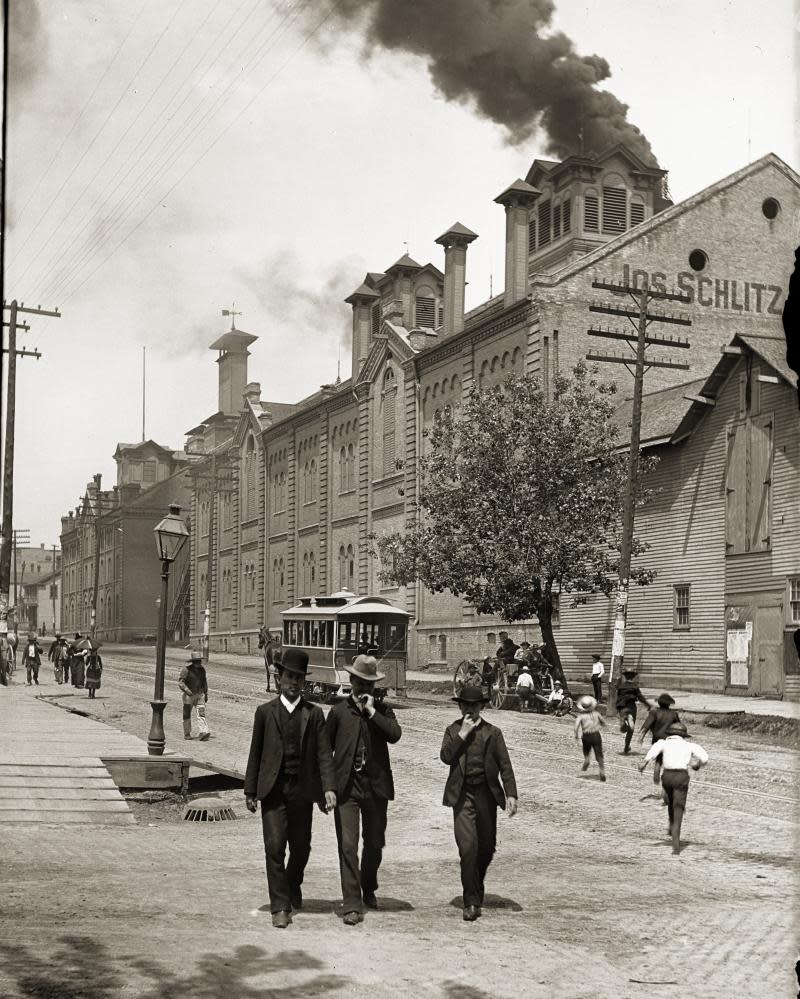 Exterior of Schlitz Brewing Company with two men and a boy in suits and hats in the foreground, Milwaukee, Wisconsin, 1888.