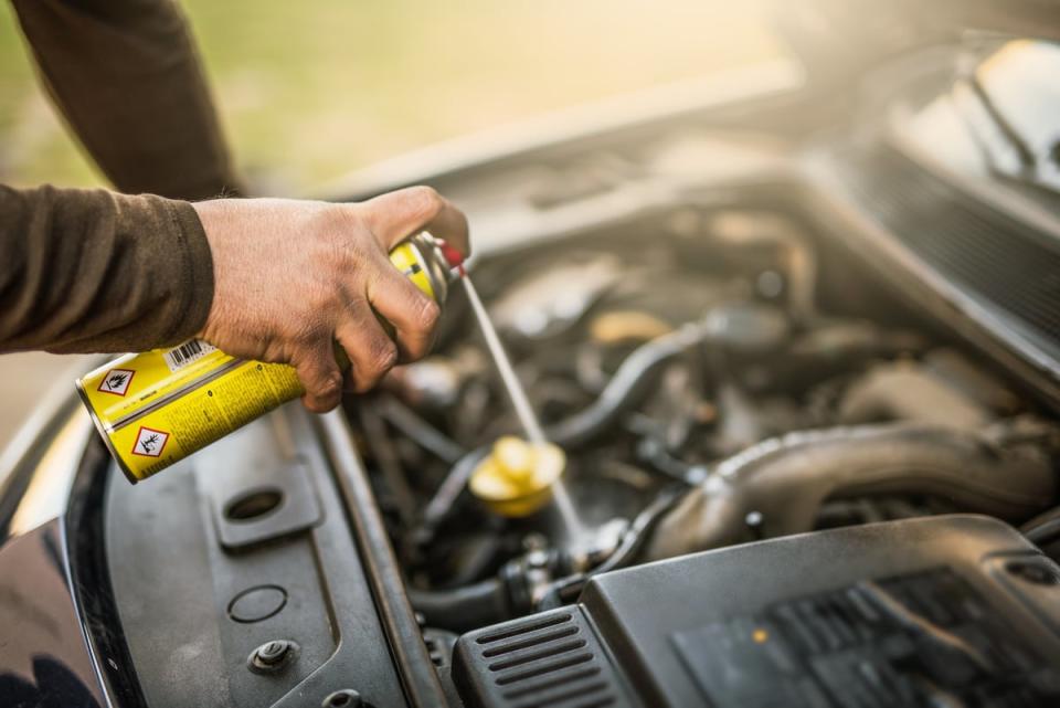 A person spraying a liquid in the inside of the hood of a car. 