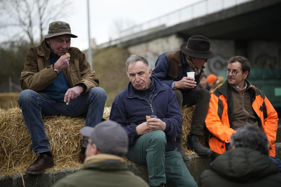 Farmers eat sandwiches as they block a highway Tuesday, Jan. 30, 2024 in Jossigny, east of Paris. With protesting farmers camped out at barricades around Paris, France's government hoped to calm their anger with more concessions Tuesday to their complaints that growing and rearing food has become too difficult and not sufficiently lucrative. (AP Photo/Christophe Ena)